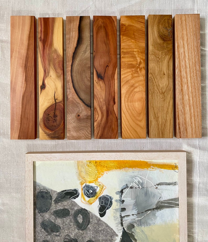 Pu&ograve; includere: Sette campioni di legno di diversi tipi, disposti orizzontalmente. I campioni di legno sono tutti di dimensioni e forma approssimativamente uguali. I campioni di legno sono tutti di colore marrone chiaro, con motivi di venatura variabili. Sotto i campioni di legno c'&egrave; una cornice bianca con un dipinto all'interno. Il dipinto &egrave; astratto e presenta colori neri, grigi e gialli.