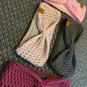 May include: Three crocheted headbands in pink, gray, and burgundy with a brown leather tag that says "Qn". Each headband has a soft, fleece lining.