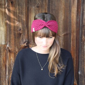 May include: A woman wearing a burgundy knitted headband with a knot on top. She is wearing a dark sweater and has long brown hair.