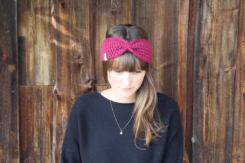 May include: A woman wearing a burgundy knitted headband with a knot on top. She is wearing a dark sweater and has long brown hair.