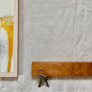 Pu&ograve; includere: Un porta chiavi in legno con finitura in legno naturale. Il porta chiavi &egrave; montato su una parete e ha un set di chiavi appese.