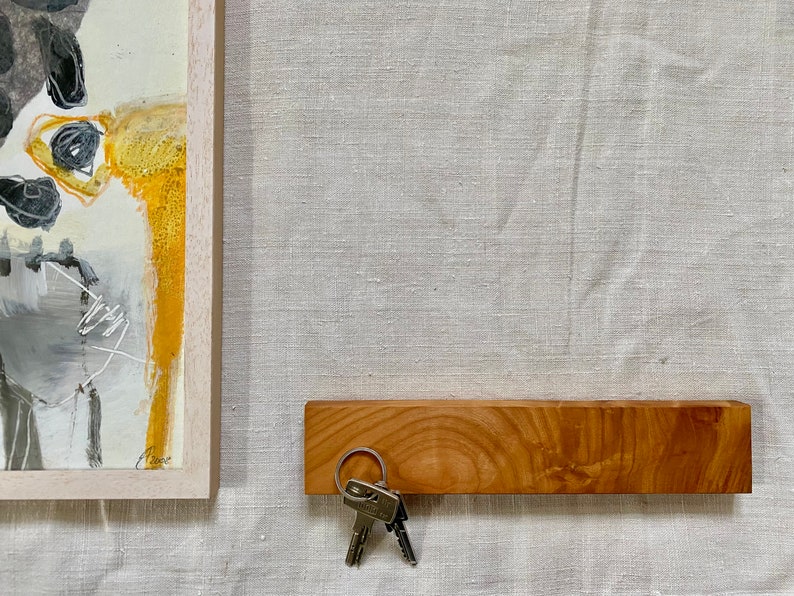 Pu&ograve; includere: Un porta chiavi in legno con finitura in legno naturale. Il porta chiavi &egrave; montato su una parete e ha un set di chiavi appese.
