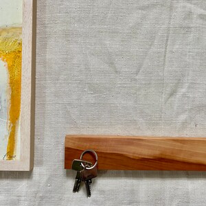 Pu&ograve; includere: Un porta chiavi in legno con finitura in legno naturale. Un set di chiavi &egrave; appeso a un anello di metallo attaccato al porta chiavi.