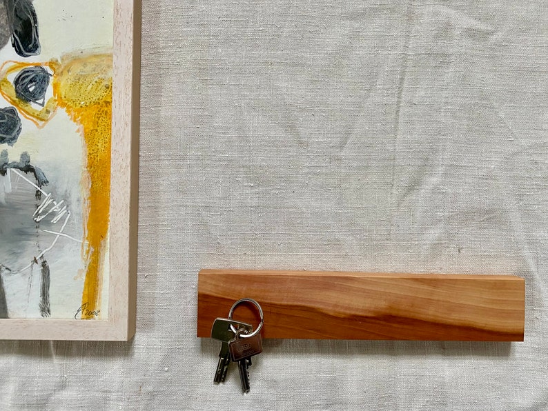 Pu&ograve; includere: Un porta chiavi in legno con finitura in legno naturale. Un set di chiavi &egrave; appeso a un anello di metallo attaccato al porta chiavi.