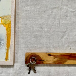 Pu&ograve; includere: Un porta chiavi in legno con una finitura in legno naturale e una tonalit&agrave; rossastra. Un set di chiavi &egrave; appeso a un anello di metallo attaccato al porta chiavi.