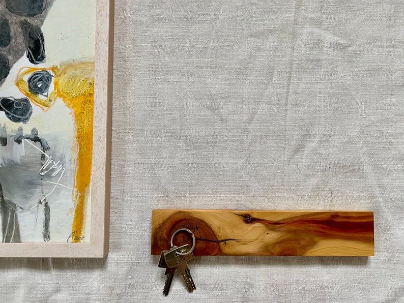 Pu&ograve; includere: Un porta chiavi in legno con una finitura in legno naturale e una tonalit&agrave; rossastra. Un set di chiavi &egrave; appeso a un anello di metallo attaccato al porta chiavi.