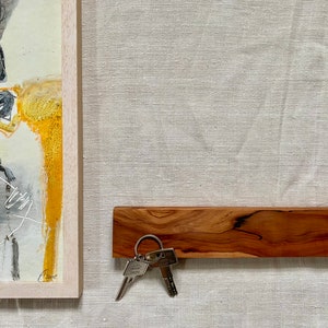 Pu&ograve; includere: Un porta chiavi in legno con una finitura in legno naturale. Due chiavi sono attaccate a un portachiavi argentato e sono appese al porta chiavi.
