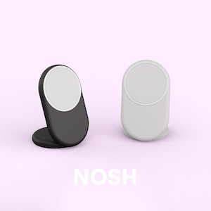 May include: Two phone stands, one black and one white, with a circular white area on top. The stands are on a light pink background, with the word "NOSH" in white letters at the bottom.