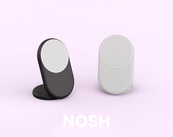 May include: Two phone stands, one black and one white, with a circular white area on top. The stands are on a light pink background, with the word "NOSH" in white letters at the bottom.