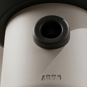May include: Close-up of a cylindrical, light gray object with a dark gray rim and a circular opening. A dark gray ring sits atop the cylinder. The word "AR77" is embossed on the side of the cylinder.