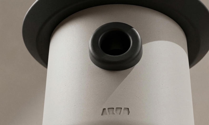May include: Close-up of a cylindrical, light gray object with a dark gray rim and a circular opening. A dark gray ring sits atop the cylinder. The word "AR77" is embossed on the side of the cylinder.