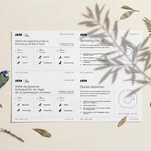 May include: A white bird species guide with illustrations and text, including entry hole sizes of 27mm, 32mm, and 37mm. A blue and green bird figurine is on the left. The guide also includes instructions for removing the lid.