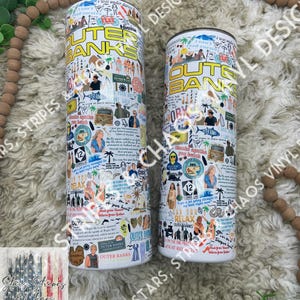 May include: Two white stainless steel tumblers with a colorful design featuring the words "Outer Banks" and various images and text from the popular TV show. The tumblers are on a brown and white fuzzy surface.