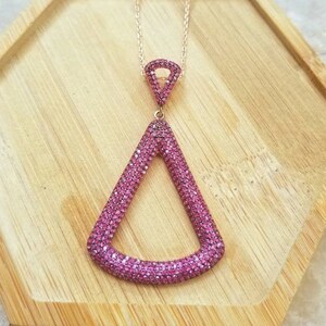 May include: A rose gold necklace with a pink crystal pendant shaped like a triangle. The pendant is set with small pink crystals.
