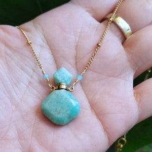 Pode incluir: Um colar de corrente dourada com um pingente de garrafa de pedra verde. A garrafa é feita de uma pedra verde claro com uma parte superior dourada.