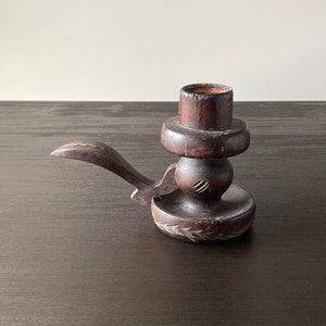 Pu&ograve; includere: Un portacandele in legno marrone scuro con un design intagliato. Il portacandele ha una piccola maniglia sul lato e una base rotonda.