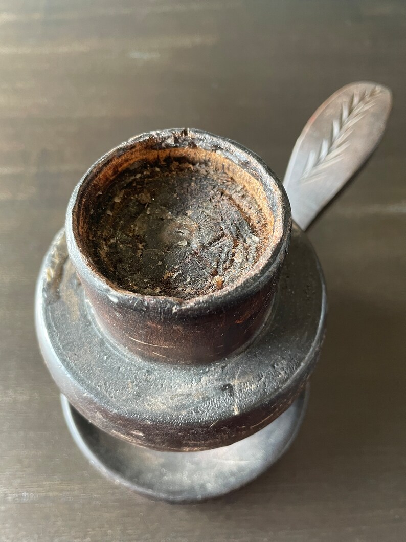 Pu&ograve; includere: Un portacandele in legno marrone scuro con una piccola parte superiore rotonda aperta e una base rotonda separata, pi&ugrave; piccola. Il portacandele ha un manico in legno intagliato con un motivo a foglia.