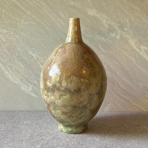 May include: A ceramic vase with a rounded body and a narrow neck, featuring a crystalline glaze in shades of golden brown, tan, and cream. The surface displays distinct circular crystal patterns throughout, creating a textured appearance.