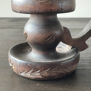 Pu&ograve; includere: Un portacandele in legno marrone scuro con un design intagliato. Il portacandele ha una base rotonda e uno stelo alto e sottile.