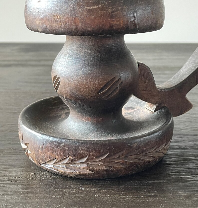 Pu&ograve; includere: Un portacandele in legno marrone scuro con un design intagliato. Il portacandele ha una base rotonda e uno stelo alto e sottile.