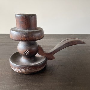 Pu&ograve; includere: Un portacandele in legno marrone scuro con un design intagliato. Il portacandele ha una base rotonda e un manico lungo.