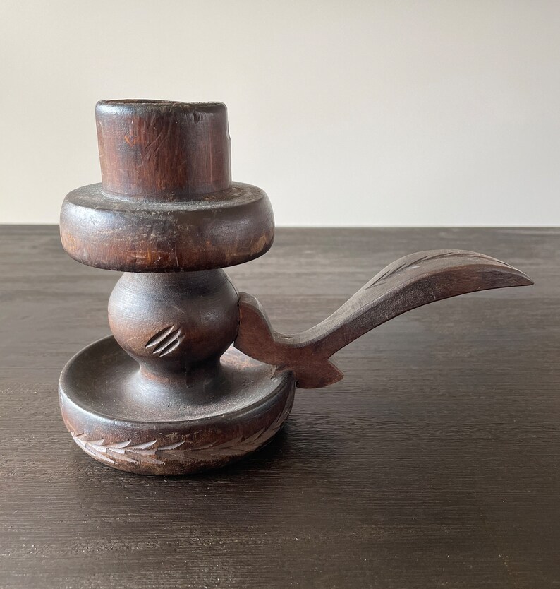 Pu&ograve; includere: Un portacandele in legno marrone scuro con un design intagliato. Il portacandele ha una base rotonda e un manico lungo.
