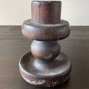 Pu&ograve; includere: Un portacandele in legno marrone scuro con una base rotonda e un design intagliato. Il portacandele ha una parte superiore cilindrica e una sezione centrale rotonda.
