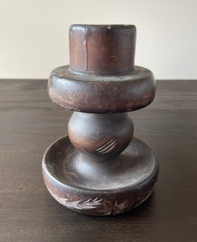Pu&ograve; includere: Un portacandele in legno marrone scuro con una base rotonda e un design intagliato. Il portacandele ha una parte superiore cilindrica e una sezione centrale rotonda.