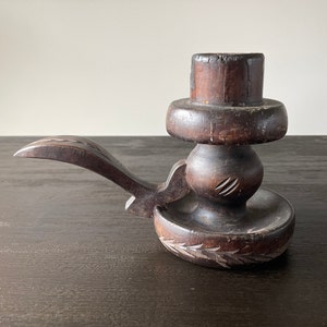 Pu&ograve; includere: Un portacandele in legno marrone scuro con un design intagliato. Il portacandele ha un manico lungo e curvo e una base rotonda.