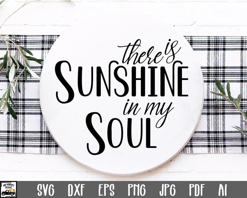 May include: A circular, white wooden sign featuring the words "there is SUNSHINE in my SOUL" in black script. The sign rests on a black and white checked surface, with foliage.
