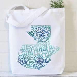 May include: White canvas tote bag with a teal and blue outline of Guatemala with a mandala design and the word "Guatemala" written in a stylized font.