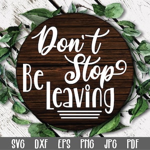 May include: A round wooden sign with the text "Don't Stop Leaving" in white lettering. The sign is surrounded by green leaves.