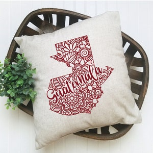 May include: A decorative throw pillow with a red outline of the country of Guatemala filled with intricate mandala designs. The word "Guatemala" is written in cursive across the outline.