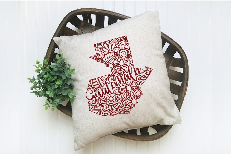 May include: A decorative throw pillow with a red outline of the country of Guatemala filled with intricate mandala designs. The word "Guatemala" is written in cursive across the outline.