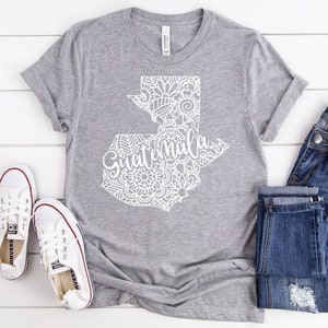 May include: A gray t-shirt with a white outline of Guatemala with a mandala design and the word "Guatemala" written inside the outline.
