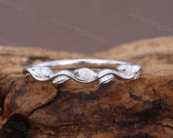May include: A delicate silver band with a vine design and marquise-shaped diamonds. The band is set on a wooden surface.