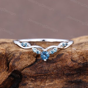 Könnte beinhalten: Ein zarter Silberring mit einem blauen Edelstein und kleineren blauen Edelsteinen auf der Ringschiene. Der Ring liegt auf einem Stück Holz.