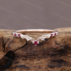 Puede incluir: Un delicado anillo de oro rosa con un diseño en forma de V. El anillo está adornado con pequeñas piedras preciosas rojas y blancas.