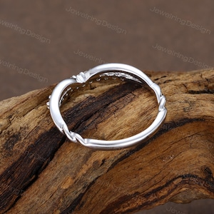 Pu&ograve; includere: Un anello d'argento con un design a fascia intrecciata. L'anello presenta una fila di piccole pietre trasparenti lungo la curva superiore. L'anello &egrave; posto su uno sfondo di legno, evidenziando il suo design elegante. &Egrave; un gioiello.