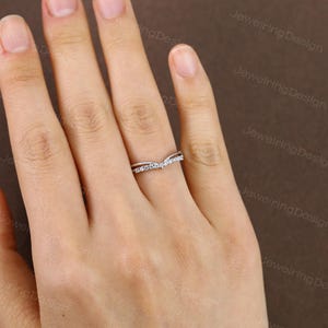 Pu&ograve; includere: Un anello color argento con un design curvo, incastonato con piccole pietre preziose trasparenti. L'anello &egrave; mostrato sulla mano di una persona, con uno sfondo neutro. Il design dell'anello &egrave; a forma di V, con le gemme incastonate lungo la curva superiore.