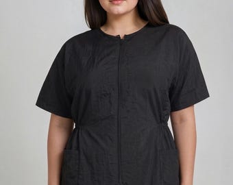 May include: Black short-sleeved top with a front zipper closure and two front pockets. The top has a cinched waist and a round neckline. The fabric has a subtle textured appearance. The model is wearing black leggings.