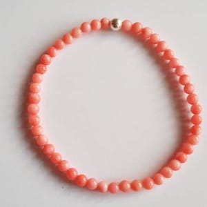 May include: A pink coral beaded bracelet with a silver bead accent.
