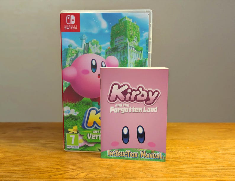 May include: A pink Nintendo Switch game case with a pink Kirby character on the front. The case is titled "Kirby and the Forgotten Land". A pink instruction manual with the same title is in front of the case.