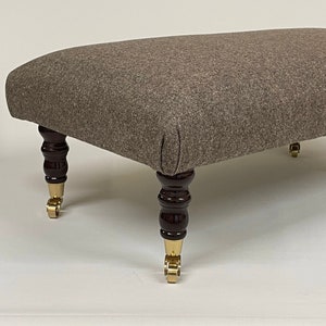 May include: A brown fabric ottoman with dark wood legs and gold castors.