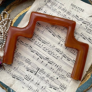 May include: A brown plastic frame with a unique shape, resting on a sheet of music with the title "Sonatine" and musical notation.
