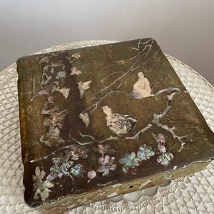 May include: A rectangular, antique wooden box with a detailed, inlaid design. The box features a bird and floral motif with iridescent mother-of-pearl accents. The box has a dark, aged finish and a scalloped edge.
