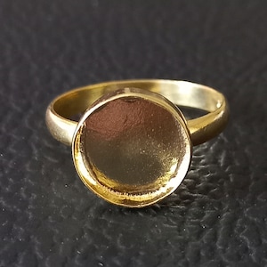 Peut inclure: Une bague en or avec une bélière ronde vide. La bague est conçue pour tenir une petite pierre ronde en cabochon.