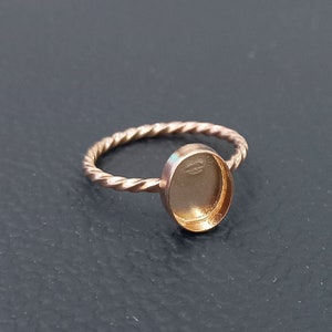 May include: A gold-toned ring with a twisted band and a round, empty bezel setting.