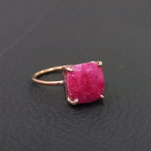 May include: A rose gold ring with a large, square-shaped, pink ruby gemstone.