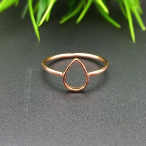 May include: A rose gold ring with a teardrop shaped cutout. The ring is on a dark gray surface.